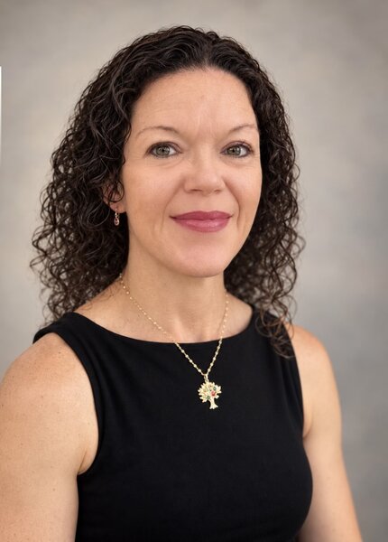 Melanie Black professional headshot smiling in a black top with a gold pendant necklace